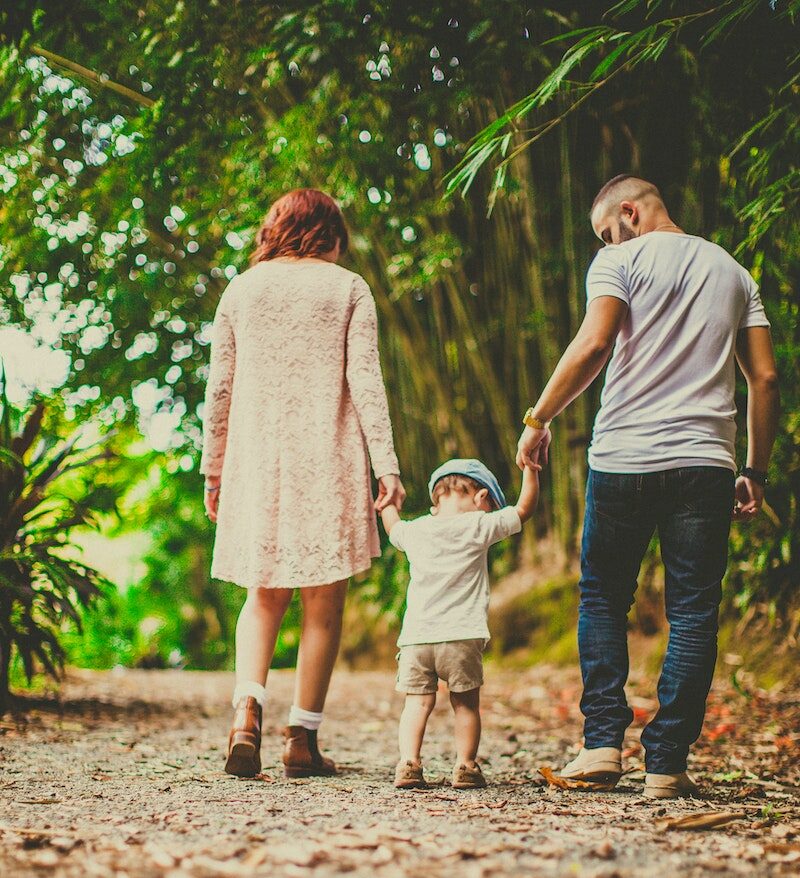 Low Angle Shot Of A Child Held by Woman and Man on On Each Hand Walking On An Unpaved Pathway Outdoors