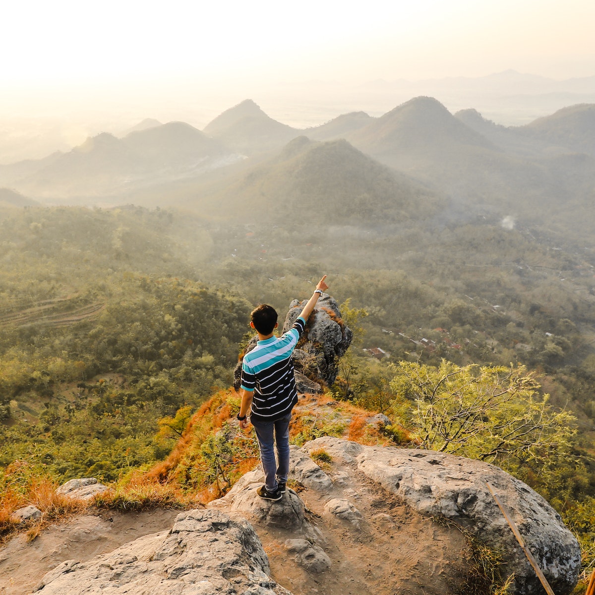 Photo of Man Standing on Rock Mountain Pointing Out Mountain